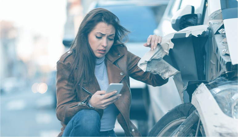mujer mirando el telefono preocupada, apoyada en un vehiculo destrozado